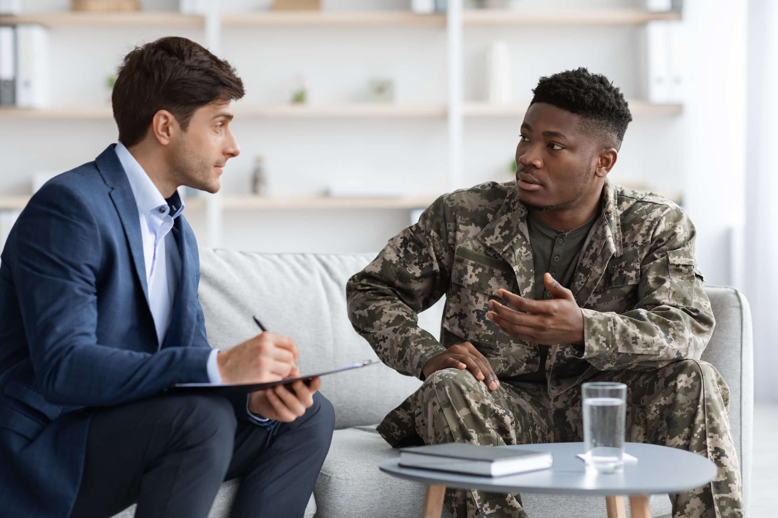 African American soldier having a conversation with a man in a suit on a couch